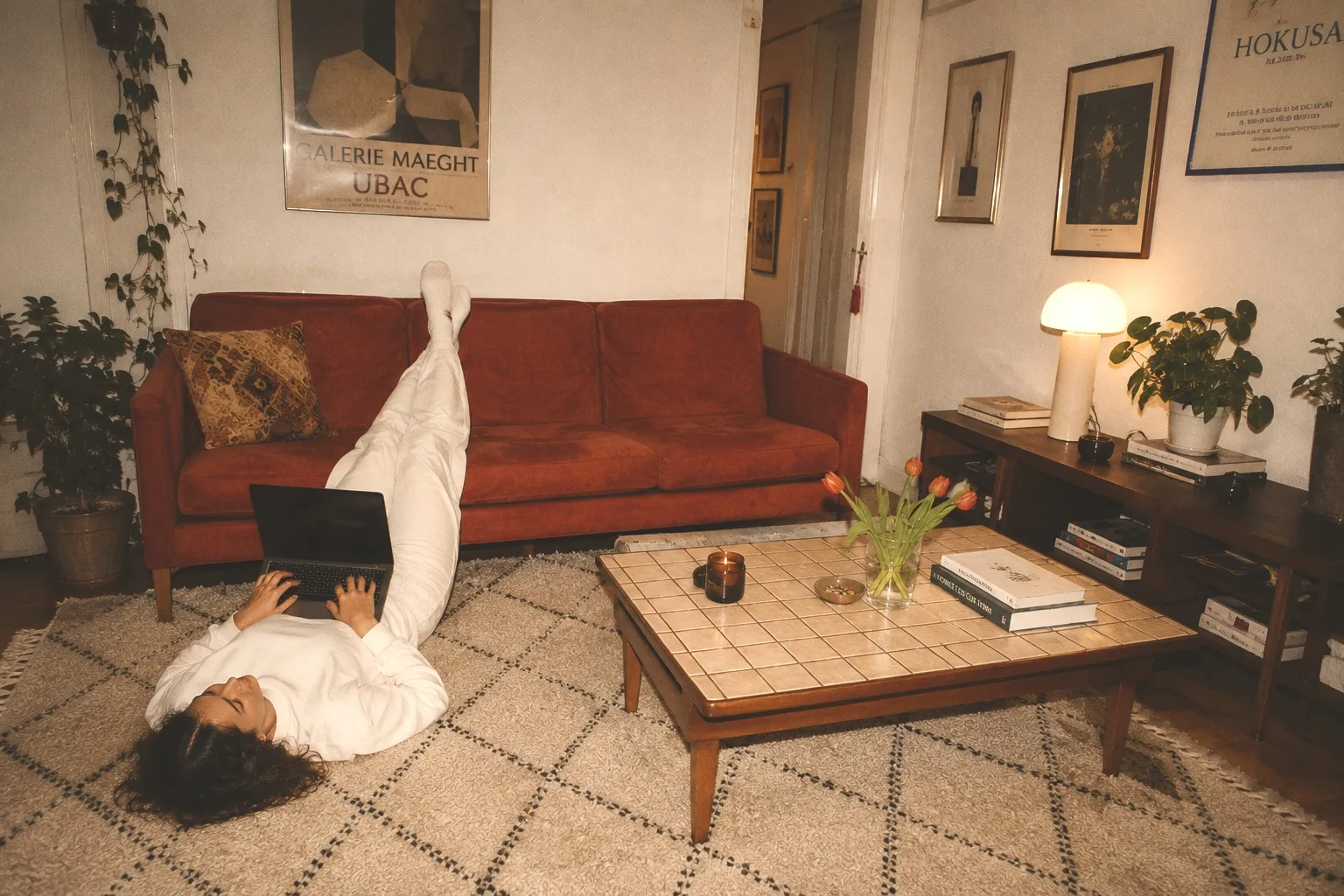 A student lying on a rug with a laptop, feet up on the couch